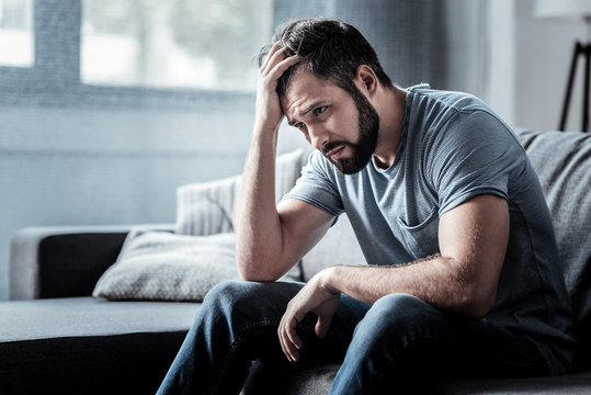 A man sitting alone on a couch, deep in low spirits