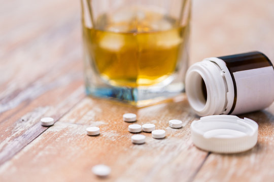 A glass of alcohol beside spilled pills on a wooden table